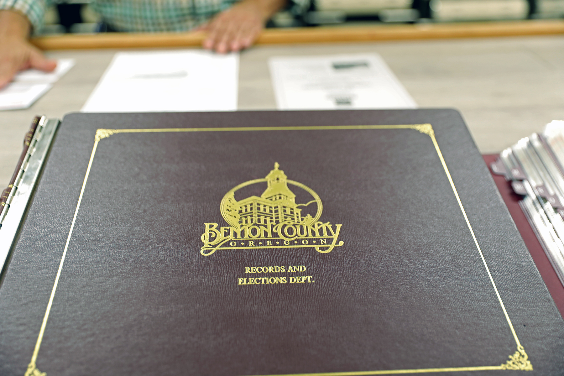 A large older brown book with gold embellishing on it in the shape of Benton County's clocktower logo. "Records And Elections Dept." reads under it.