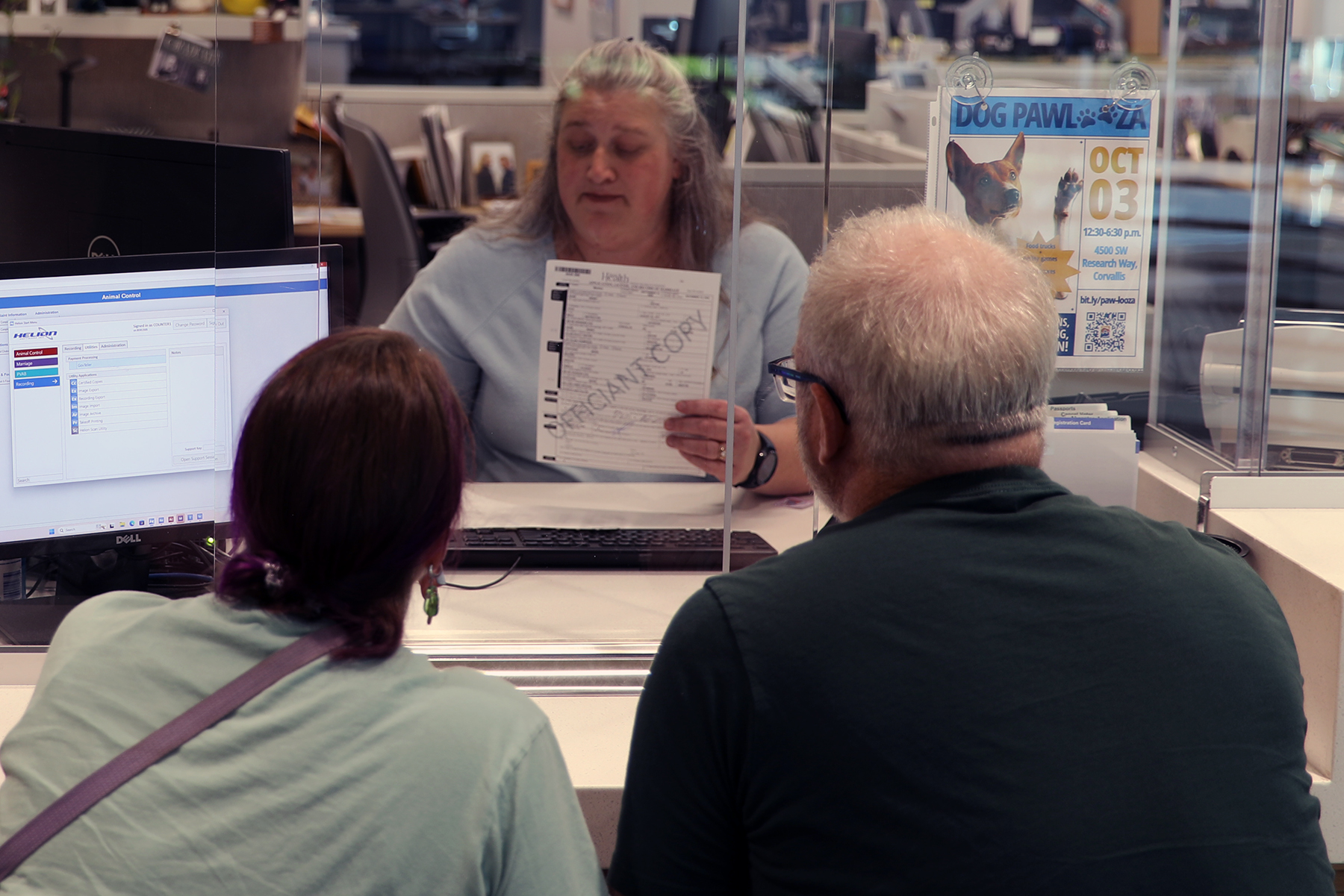A couple sits at the Records and Elections service counter processing their marriage license, being helped by an employee of the department behind the counter.